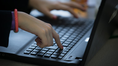 o mana cu bratara rosie scrie pe tastatura unui laptop