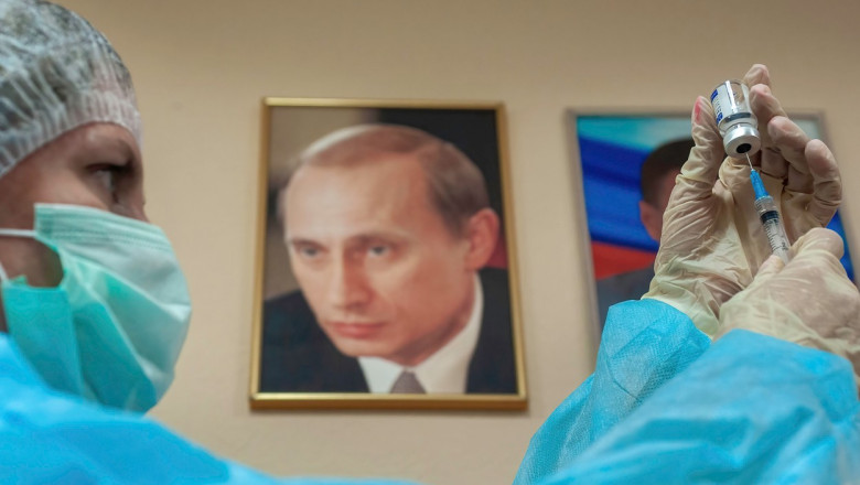 O asistentă pregătește o doză de vaccin pentru vaccinare, pe perete aflându-se un portret al lui Vladimir Putin