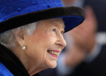Elisabeta a II-a, din profil, cu pălărie albastră, zâmbește