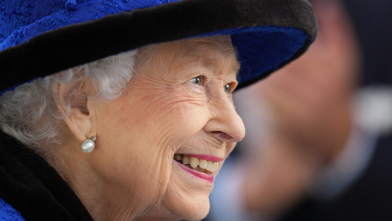 Elisabeta a II-a, din profil, cu pălărie albastră, zâmbește