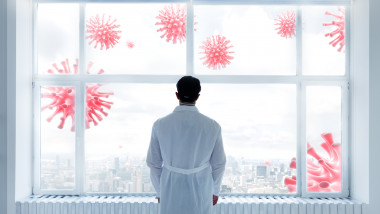 medic priveste pe geamul dincolo de care sunt reprezentari grafice ale coronavirusului