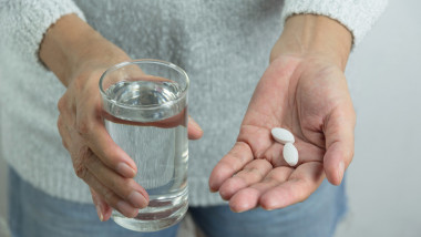 Woman holds in hands the medicine pills and a glass of water.