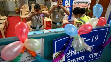doi oameni gesticulează în spatele unei tejghele ornate cu baloane, la un centru de vaccinare din India, în octombrie 2021, după administrarea a un miliard de doze de vaccin anti-covid