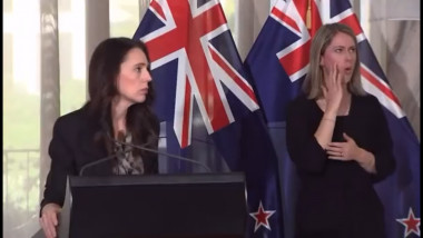 Jacinda Ardern cu steaguri ale Noii Zeelande în spate, la un pupitru cu microfon