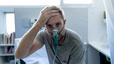 pacient cu masca de oxigen sta in sezut cu mana la cap