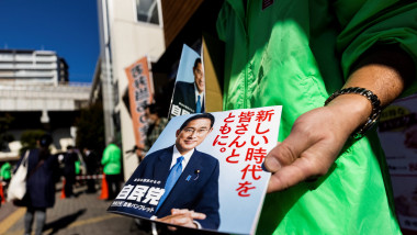 O femeie cu geacă verde ține în mână un pliant electoral cu prim-ministrul Japoniei Fumio Kishida