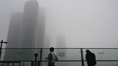 Two men stands next to a glass wall on a balcony on a polluted day in Beijing on November 5
