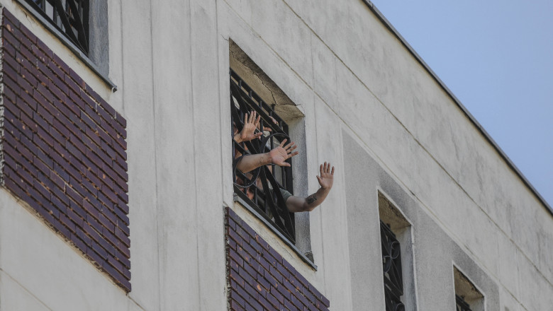 detinuti care fac cu mana printre gratiile unei ferestre a penitenciarului rahova