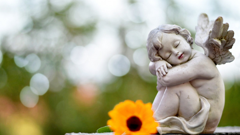 statuie a unui inger pazitor care doarme langa care este pusa o floare, pe un mormant