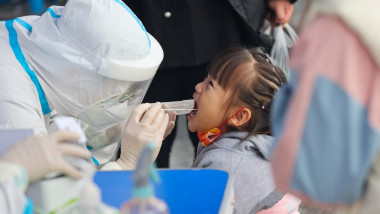 fetiță testată anti covid de un asistent in combinezon