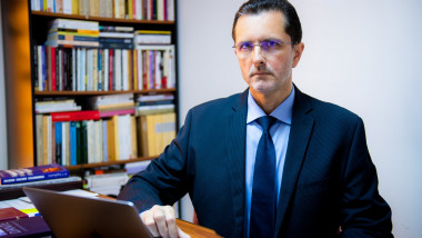 Vasile Bănescu cu ochelari, cistum, la birou cu computer