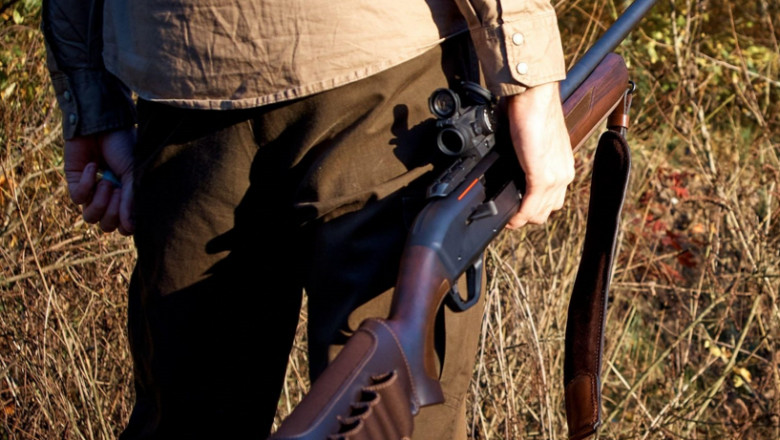 Un bărbat aflat pe câmp ține în mână o pușcă de vânătoare.