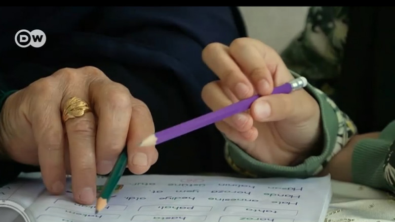mainile unei femei si ale unei tinere care tin in mana creioane si urmaresc scrisul pe o carte