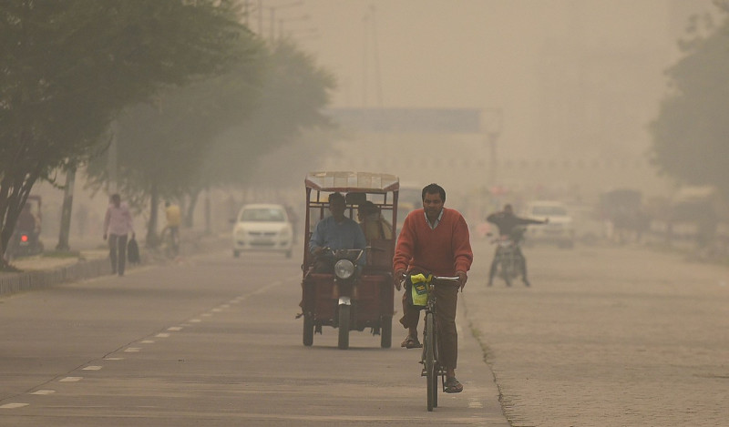 Oameni care merg pe o stradă din New Delhi, în fumul gros produs de arderea de deșeuri