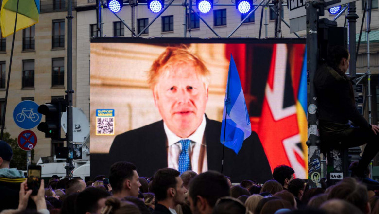 Boris Johnson pe un ecran mare, oameni se uita la el, se vede si steagul marii britanii