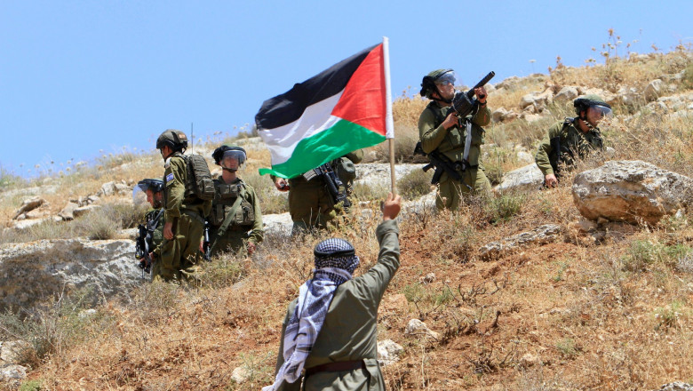 Soldații israelieni și un protestatar cu steagul Palestinei