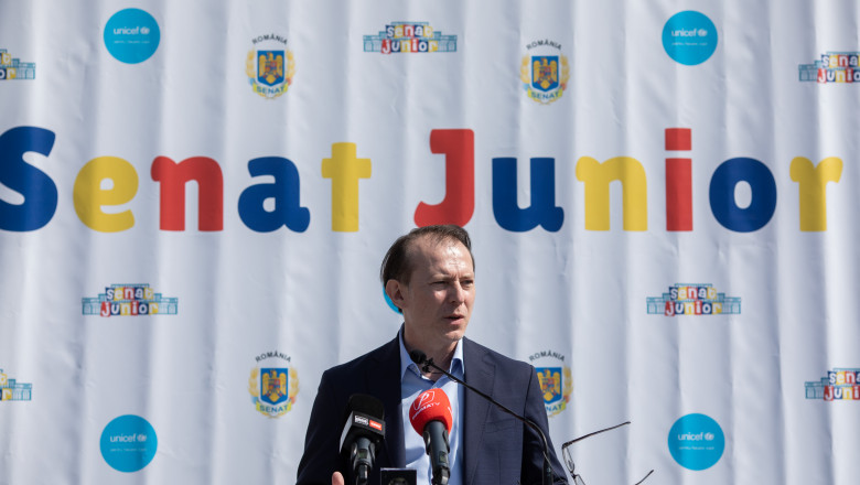 președintele Senatului, Florin Cîțu, vorbește la microfon în fața unui panou pe care scrie „Senat junior”