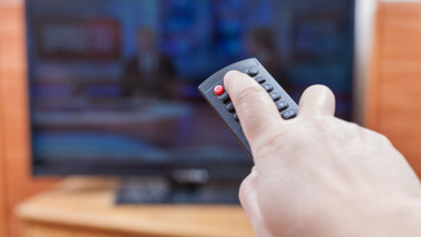 Hand turns on News on TV by remote control