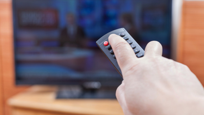 Hand turns on News on TV by remote control
