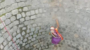 O femeie escaladează peretele unei fântâni aproape secate pentru a lua apă