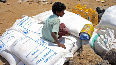Copil stă pe un sac cu ajutoare al Programului Alimentar Global din Yemen