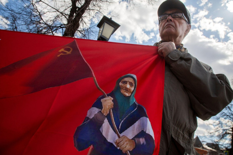 Moscow, Russia. 1st May, 2022. A man holds a banner with a portrait of the Ukraininan babushka with a Soviet Flag during a rally of the Russian Communist Party supporters marking International Workers' Day in Teatralnaya Square in central Moscow, Russia.