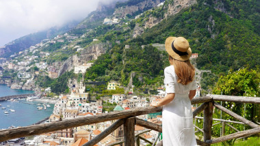 Peaceful woman with white dress and hat enjoying natural landscape from terrace on Amalfi Coast, Italy. Panoramic view. Banner.