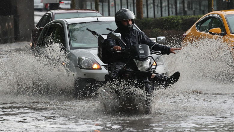 un motociclist merge prin apa in fata unor masini ridicand picioarele sus