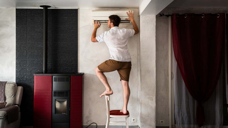 A man on a chair sticks his head against the air-conditioning to try and cool down