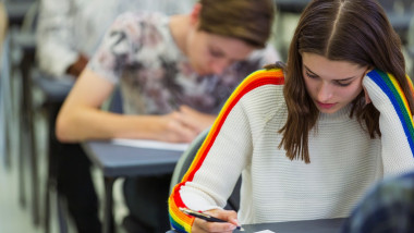 Focused high school girl student taking exam at desk in classroom