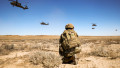 Soldat american privește la mai multe elicoptere Black Hawk care zboară deasupra sa în cadrul unui exercițiu miiltar