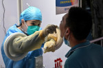 un bărbat îmbrăcat în costum de protecție testează un pacient pentru Covid-19