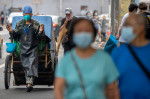 Trecători în Beijing și un bărbat cu mască care trage un căruț acoperit
