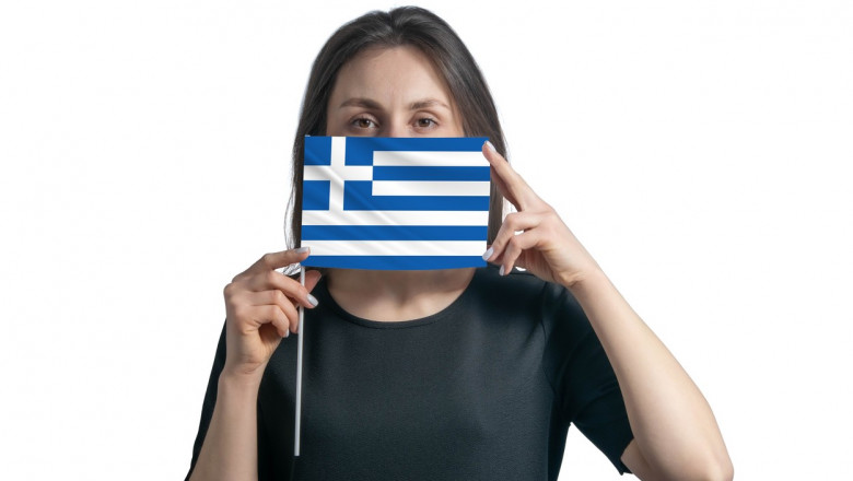 femeie care tine in dreptul gurii si al nasului un steag al greciei