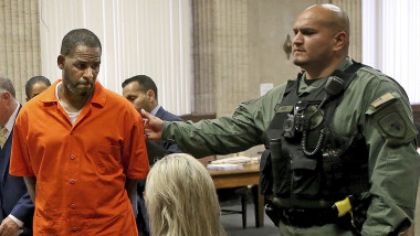 R. Kelly in uniforma portocalie de detinut, condus de un gardian in sala de judecata