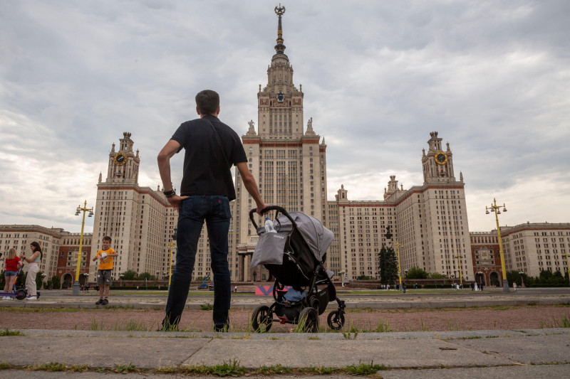 A man with a baby stroller looks at the Moscow State University high-rise building on Vorobyovy Gory (Eng:Sparrow Hills) in the center of Moscow, Russia