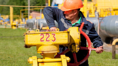 muncitor gazprom cu casca de protectie portocalie inchide robinet mare de gaz la o conducta galbena