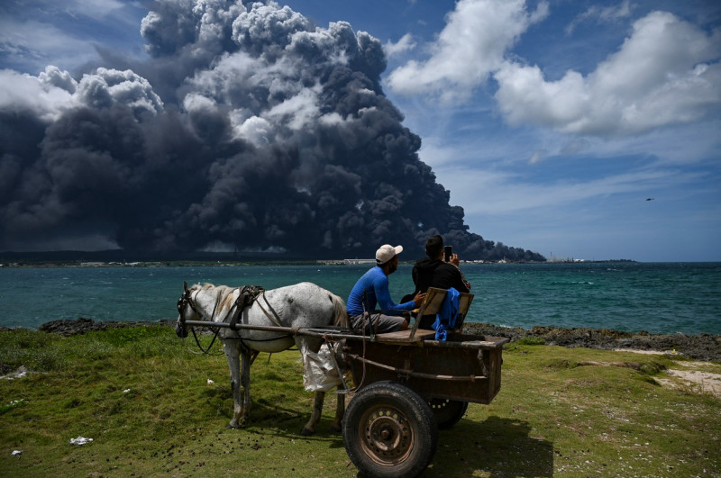 oameni într-o căruță privesc în depărtare la norul uriaș și gros de fum rezultat din incendiul de la spațiul de stocare a petrolului din Matanzas, Cuba