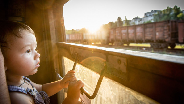 copil care priveste pe geamul trenului la un alt tren cu marfa