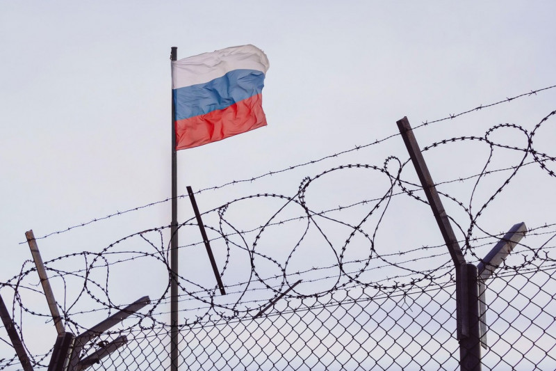 View of russian flag behind barbed wire against cloudy sky. Concept anti-Russian sanctions. A border post on the border of Russia. cancel culture Russ