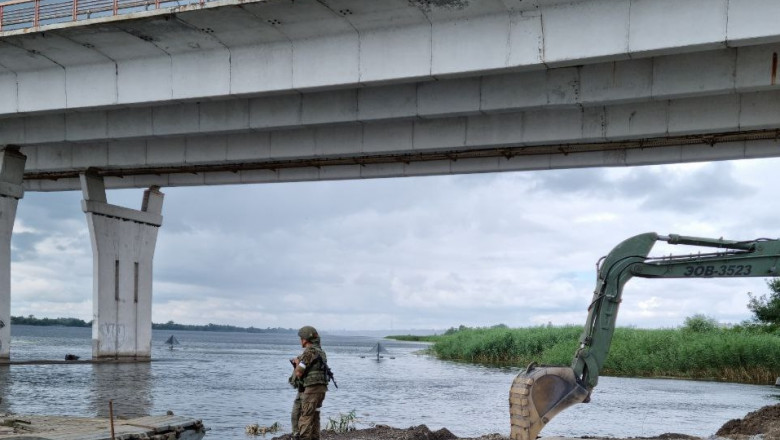 un soldat rus și un excavator la punctul de trecere cu bacul la podul Antonovski de la Herson