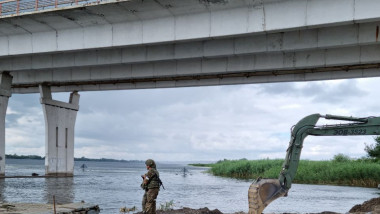 un soldat rus și un excavator la punctul de trecere cu bacul la podul Antonovski de la Herson