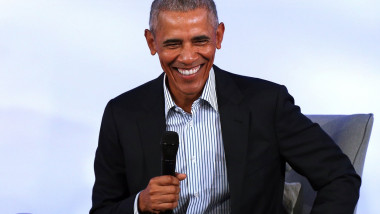 Barack Obama rade cu un microfon in mana