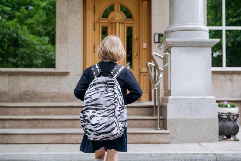 Rear view of a schoolgirl going to school with a school bag.