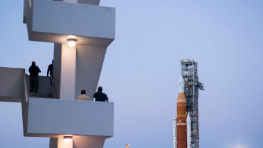 oameni aflați pe o scară privesc spre racheta lansatoare SLS care va propulsa nava Orion spre Lună în cadrul misiunii NASA Artemis 1