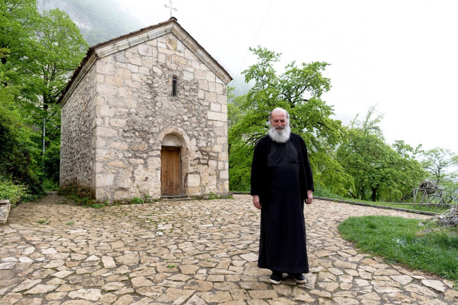 Portrait of a Monk in a black cassock in front of a chapel, Georgia
