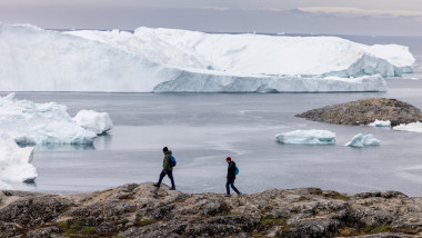 Visitors walk along a ridge overlooking icebergs floating in Disko Bay, Ilulissat, western Greenland