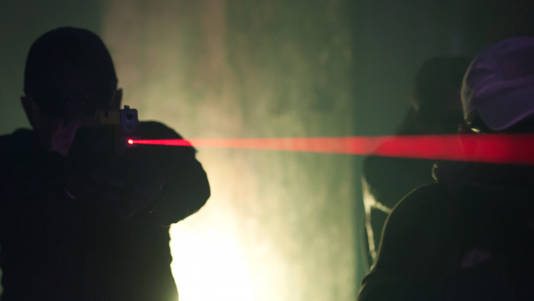 siluete ale unor bărbați care țintesc cu pistolul cu ajutorul unui dispozitiv laser