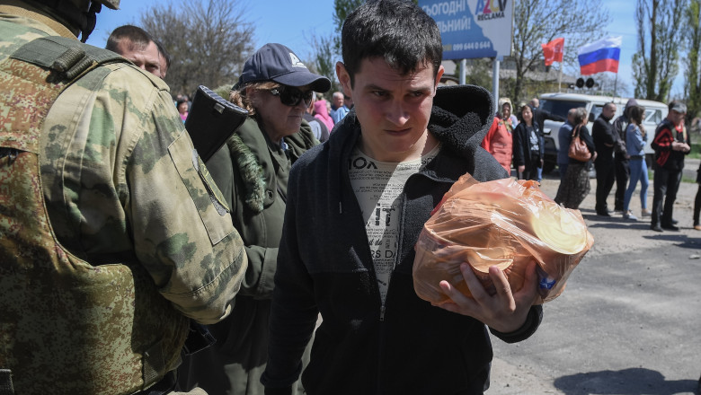 A man carries humanitarian aid in Berdyansk, Zaporozhye region, printre soldati inarmati