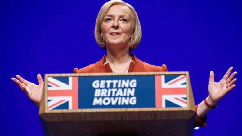 Liz Truss la un podium inscripționat cu textul Getting Britain movement peste steagul regatului unit